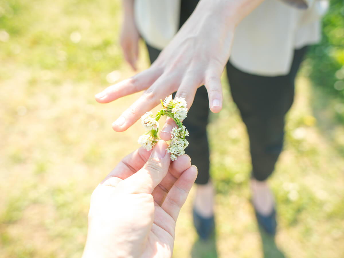 左手の薬指に花で作った指輪を彼女に着けてあげる男性